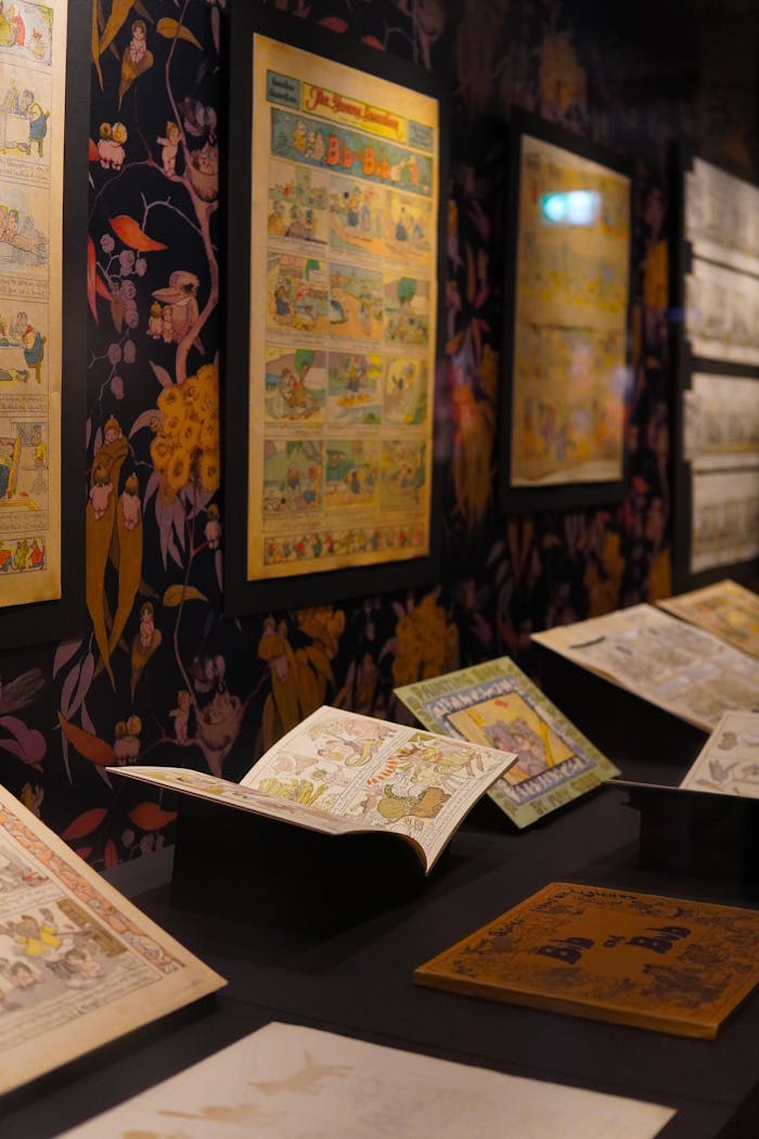 Vintage comics displayed in a well-lit museum setting with floral wallpaper.